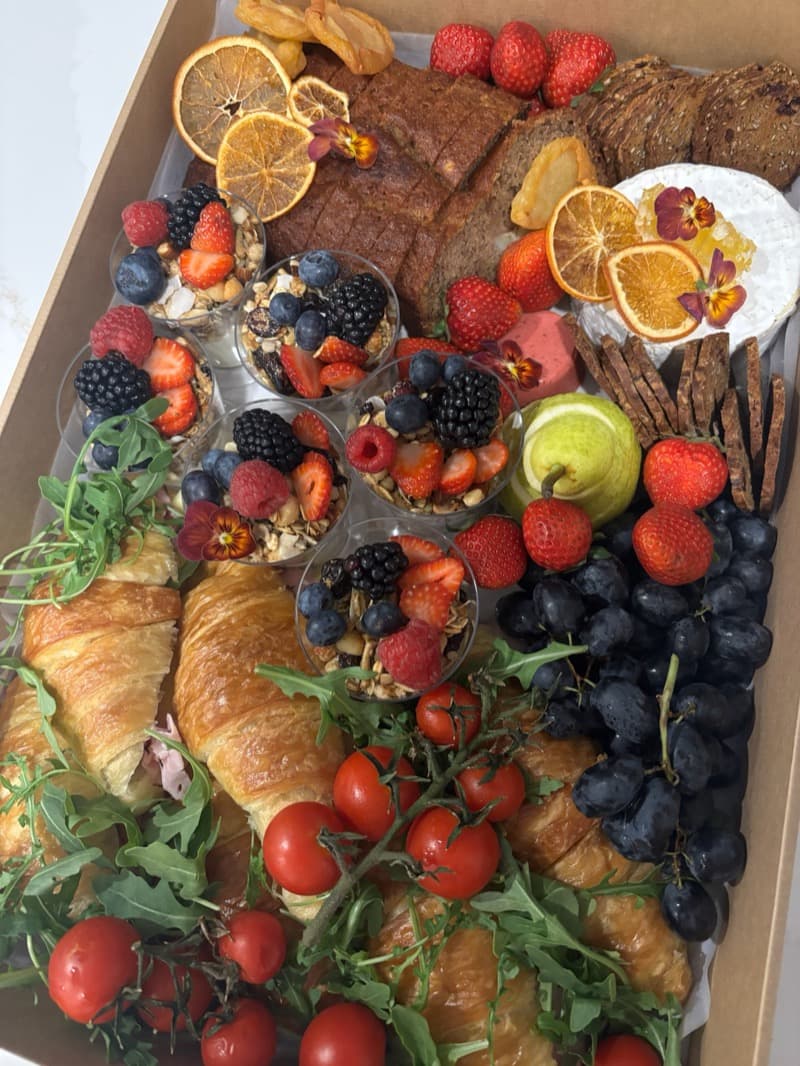 Corporate morning tea box with golden croissants, house-made banana bread, seasonal fruit, granola parfait cups, and brie