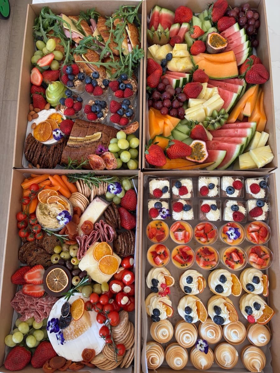Overhead view of a brunch grazing box with golden croissants, granola parfait cups, fresh berries, grapes, crackers, and brie