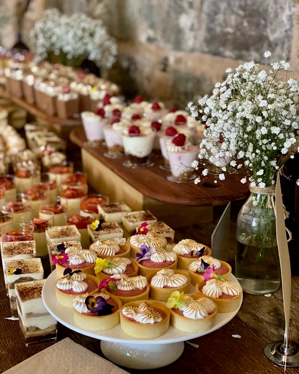 Wedding dessert table with lemon meringue tarts, tiramisu slices, raspberry panna cotta cups, and baby's breath florals at a rustic stone venue