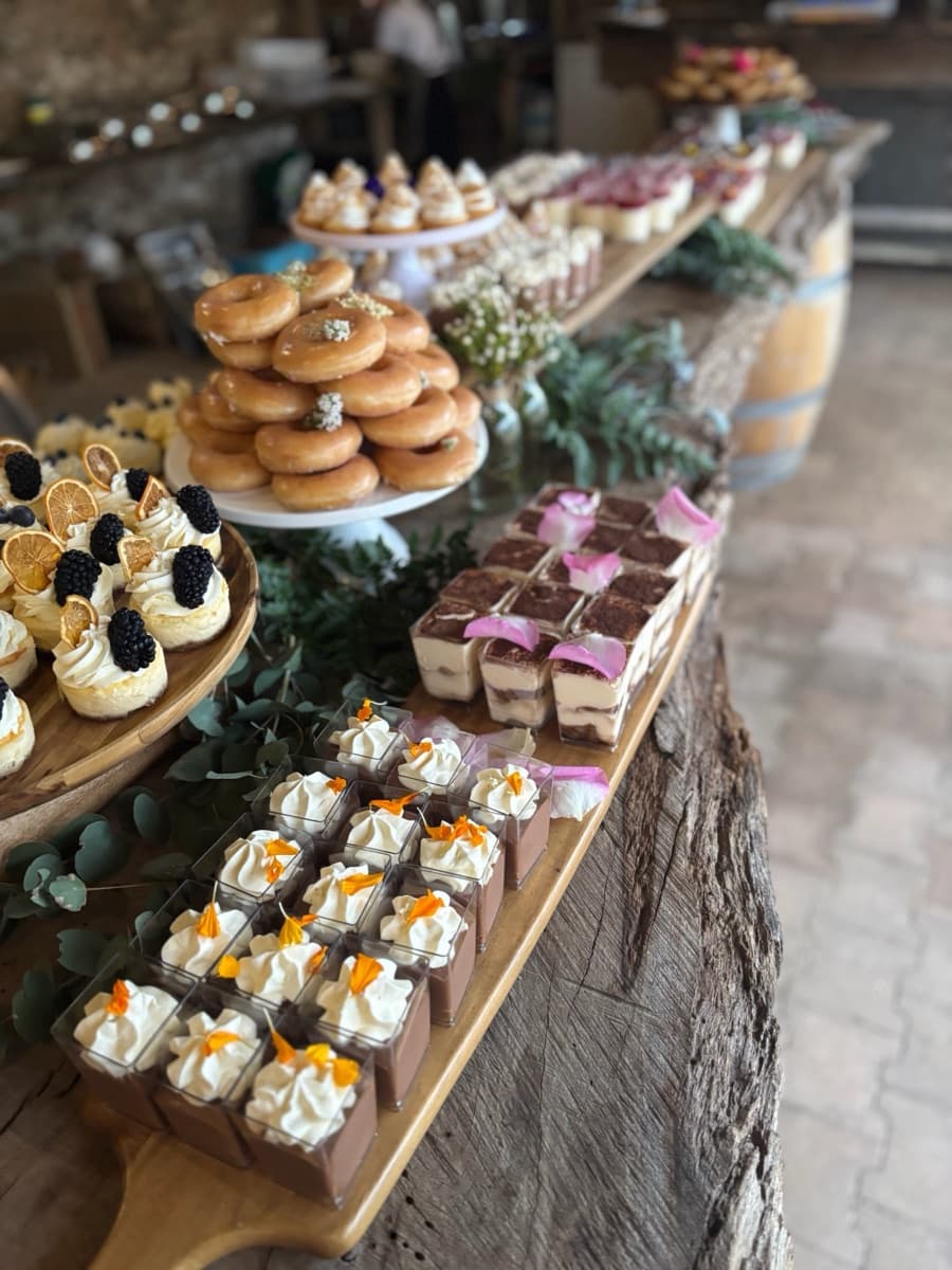 Rustic wedding dessert bar with tiramisu, mousse cups, doughnuts, and eucalyptus on wine barrels