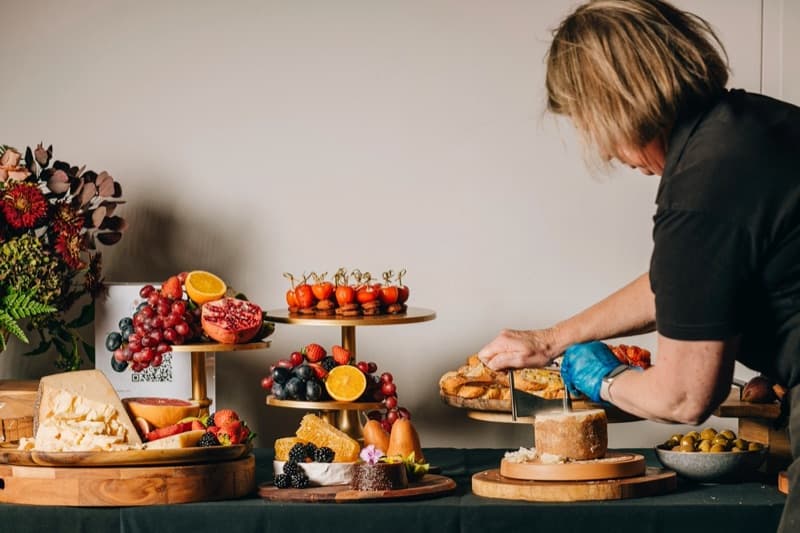 Artisan cheese board with grapes, strawberries, and honeycomb beside a floral arrangement