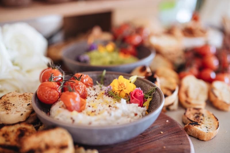 Whipped ricotta with roasted cherry tomatoes and edible flowers beside grilled sourdough rounds