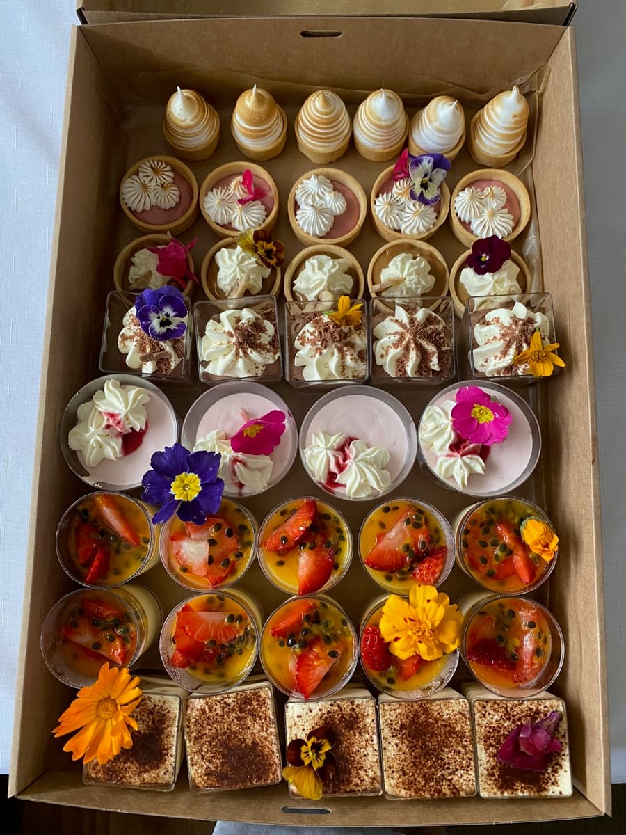Overhead Event Gourmet dessert box with lemon meringue tarts, mini cheesecakes, mousse cups, fruit tarts, and tiramisu