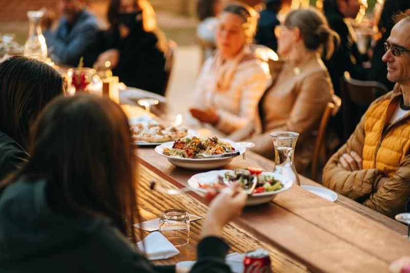 Guests enjoying plated meals at a long timber table during a warm outdoor Adelaide wedding reception at golden hour
